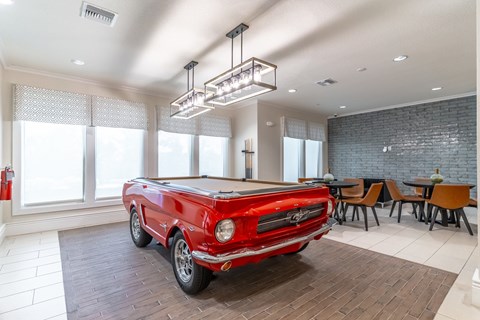 A red vintage car is parked in a spacious room with a dining table and chairs.