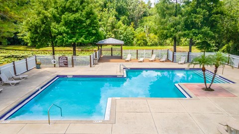 a swimming pool with chairs around it and trees in the background