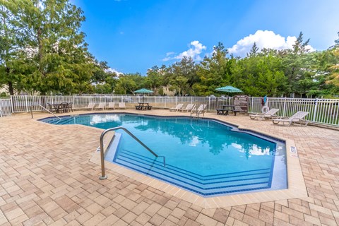 a resort style pool with chairs and umbrellas in a yard with trees