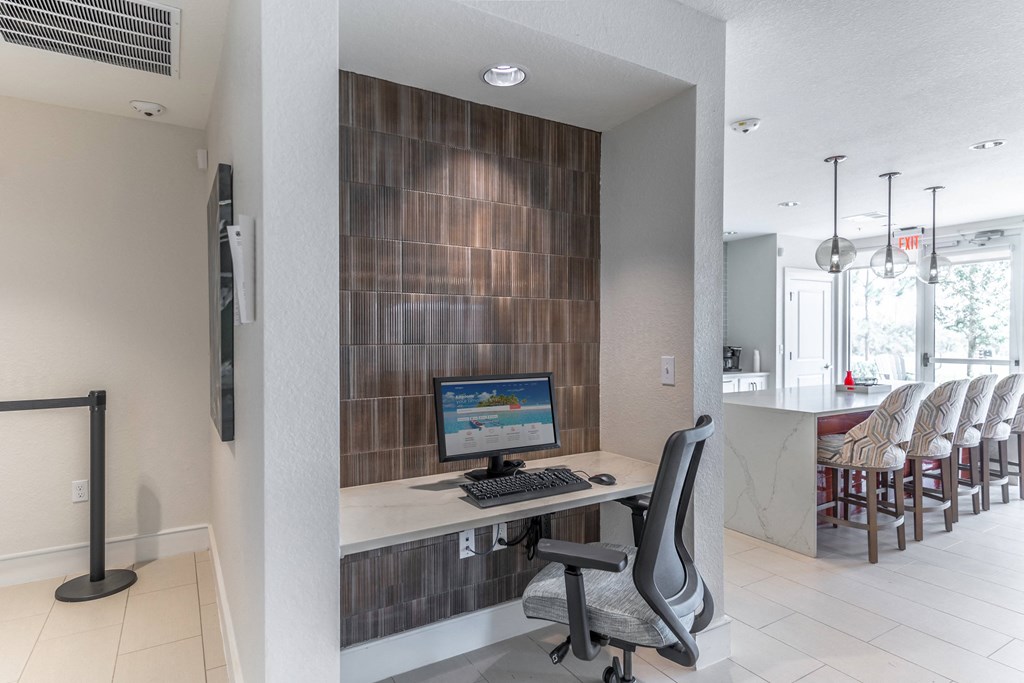 a desk with a computer in a room with a kitchen in the background