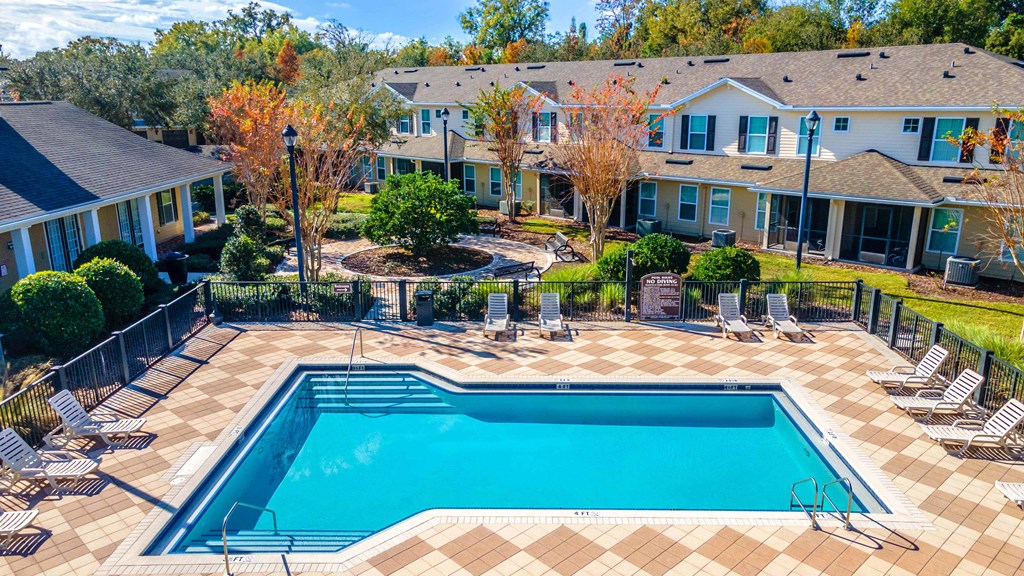 A swimming pool surrounded by a fence and chairs in a residential area.