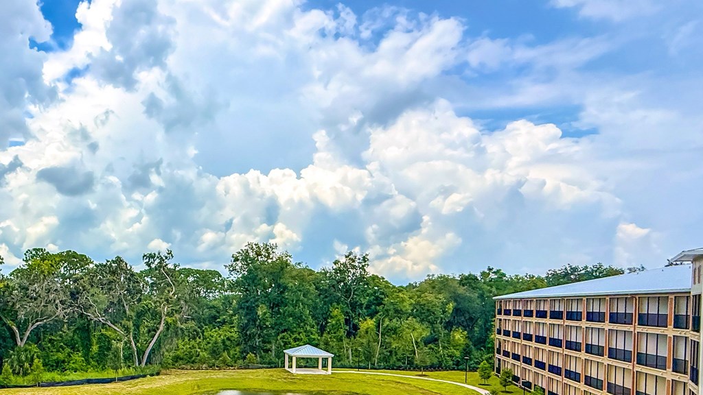 A large building is situated on a grassy area with a gazebo and trees in the background.
