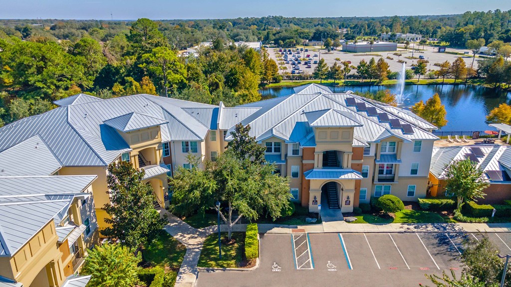 A large building with a blue roof is surrounded by trees and a parking lot.