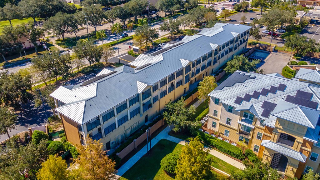 A large building with a grey roof is surrounded by trees and other buildings.