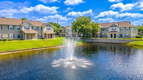 A fountain in the middle of a pond in front of apartment buildings.