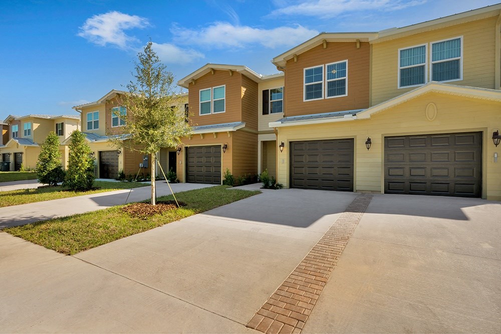 a house with two garages and a tree in the middle of a driveway