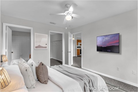 A bedroom with a bed, pillows, a ceiling fan, and a painting on the wall.
