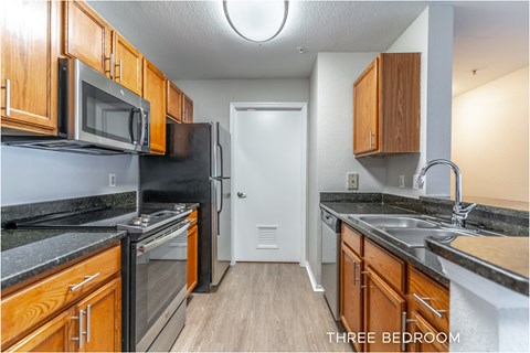 A kitchen with a refrigerator, microwave, oven, and sink.