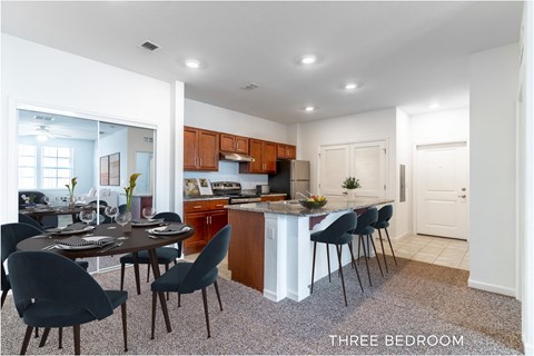 A kitchen with a dining table and chairs in a three bedroom apartment.
