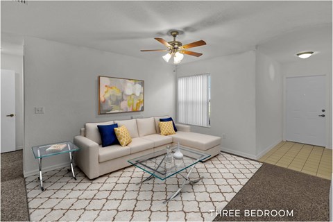 A living room with a beige couch, a glass coffee table, and a ceiling fan.