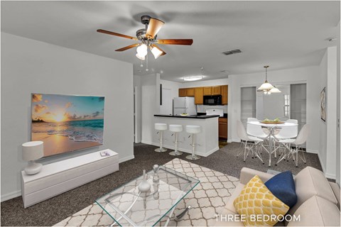 A living room with a glass coffee table and a painting of a sunset on the wall.