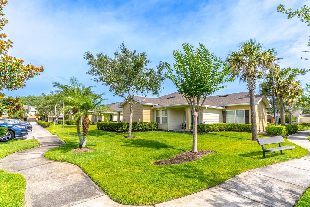 a park with a bench and trees in front of a house