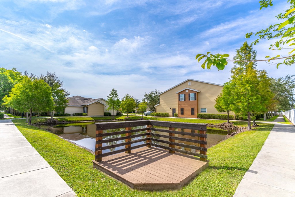 a wooden bridge over a pond with houses in the background