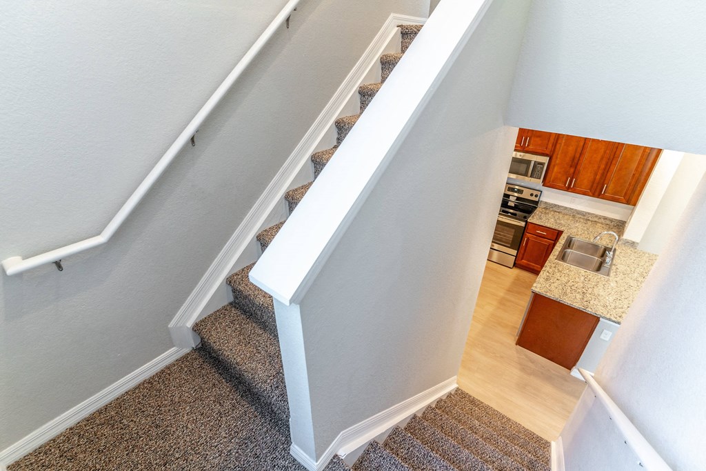 a view from the top of the stairs looking down into the kitchen and living room