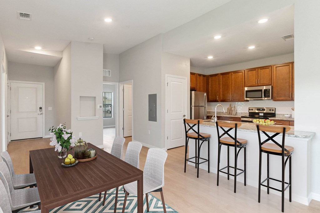A kitchen with a table and chairs in the foreground and a countertop with a microwave and oven in the background.