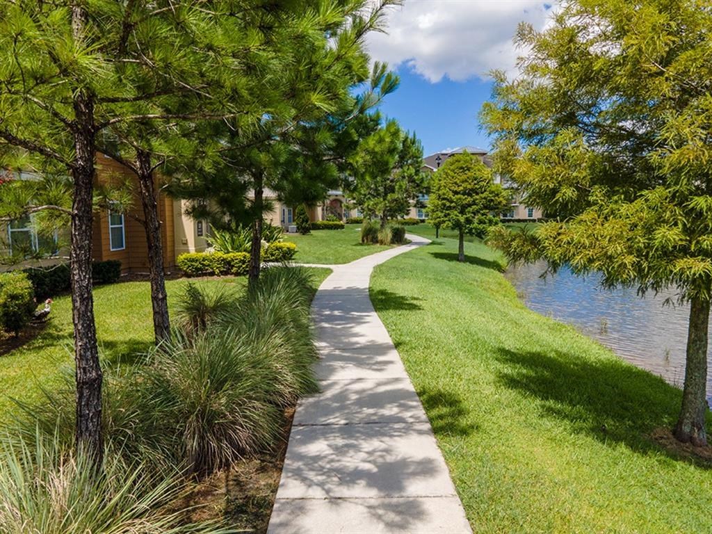 a sidewalk leading to a body of water with houses in the background