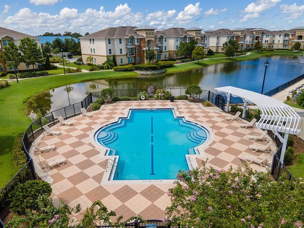 a swimming pool with a bench and chairs around it in front of a lake and apartment buildings