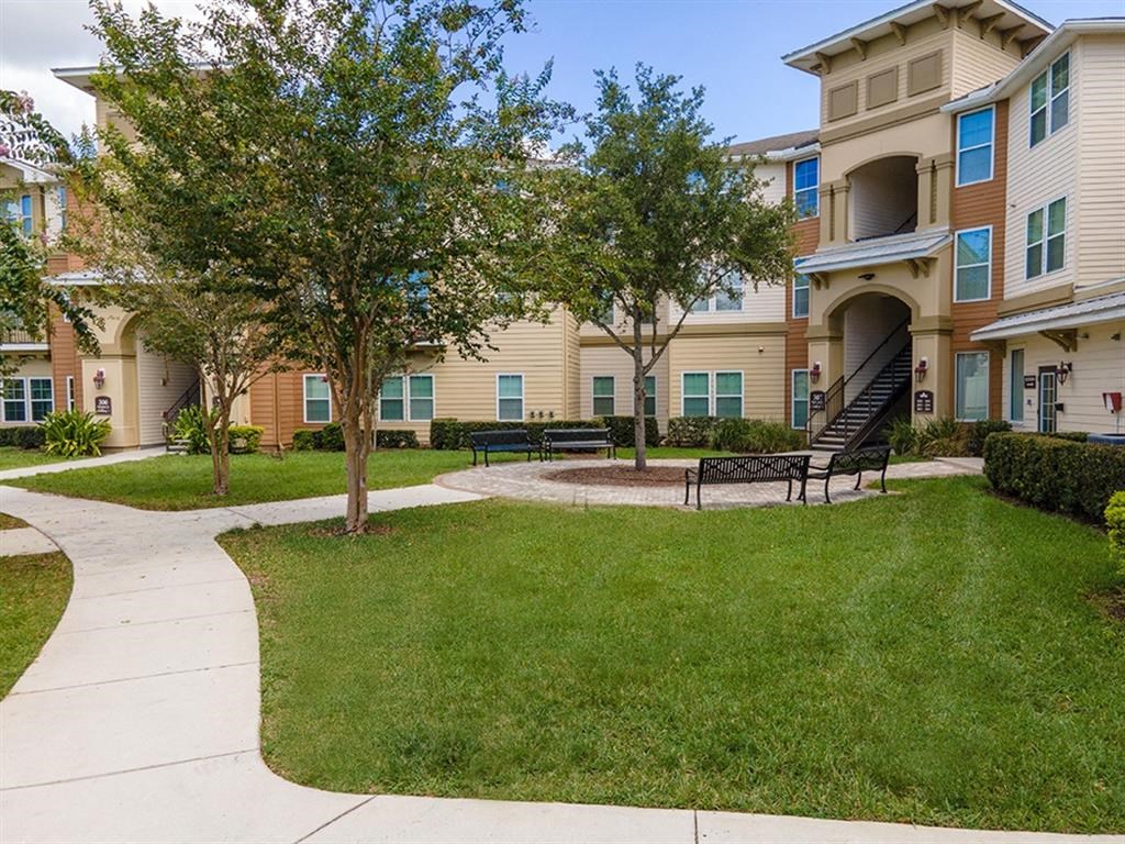 a grassy area with benches and trees in front of an apartment building