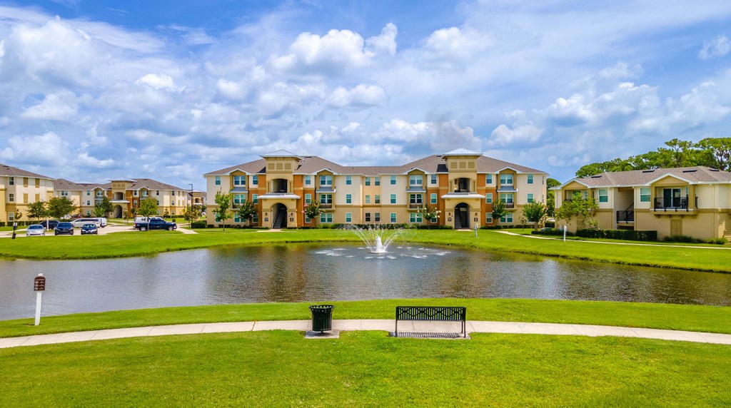 a fountain sits in the middle of a pond in front of an apartment complex