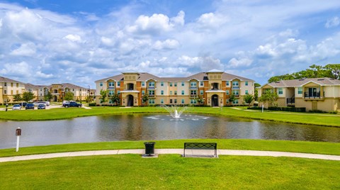 a fountain sits in the middle of a pond in front of an apartment complex