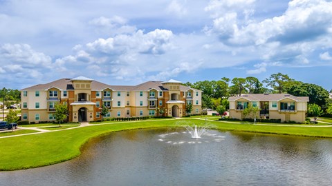 a fountain sits in the middle of a pond in front of an apartment complex