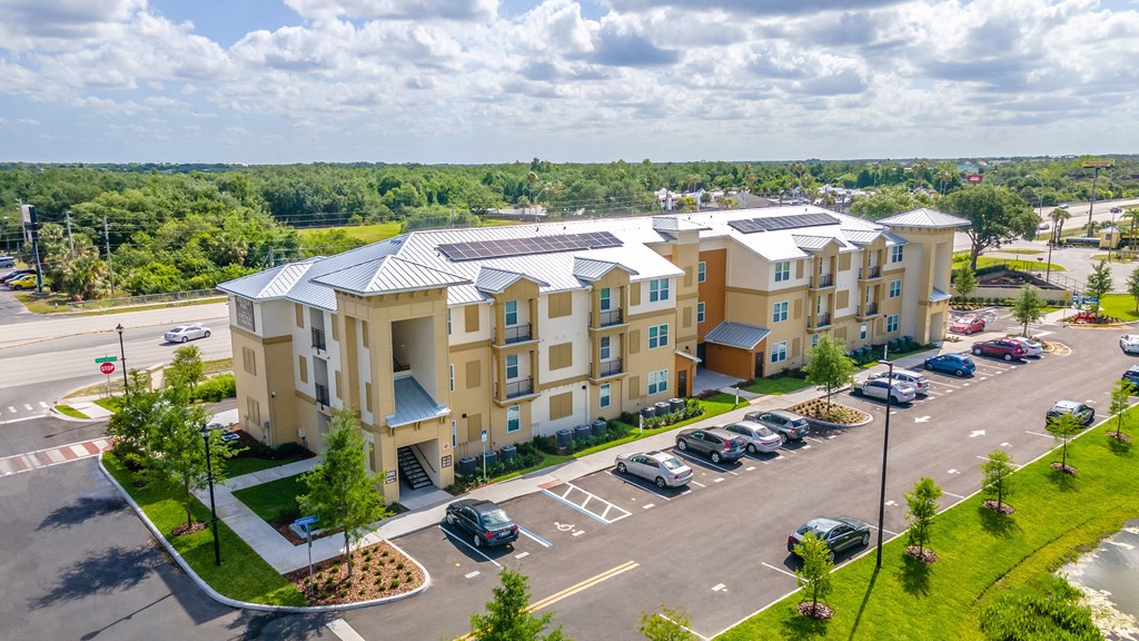 an aerial view of a large apartment complex with a parking lot and trees in the background