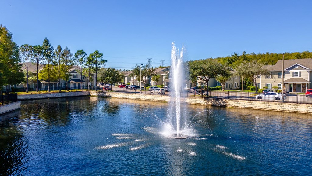 a fountain in a pond with houses in the background