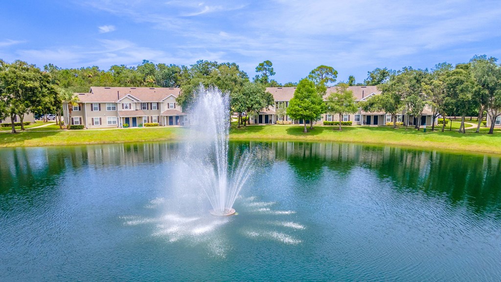 a fountain in the middle of a pond with apartment buildings in the background