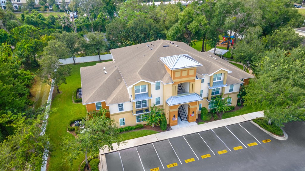 an aerial view of a large yellow house with a parking lot and trees