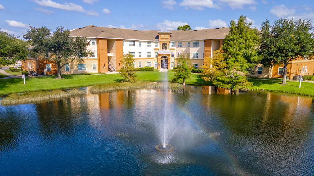 a fountain sits in the middle of a pond in front of a building