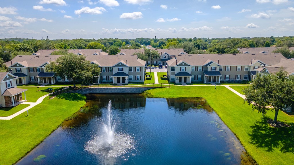 a fountain in the middle of a pond with houses in the background