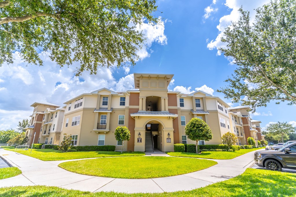 A large, beige apartment building with a green lawn in front.