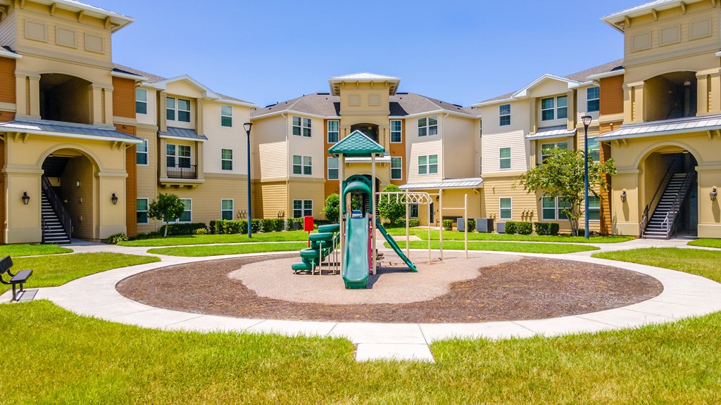 A playground area with a green slide is surrounded by apartment buildings.