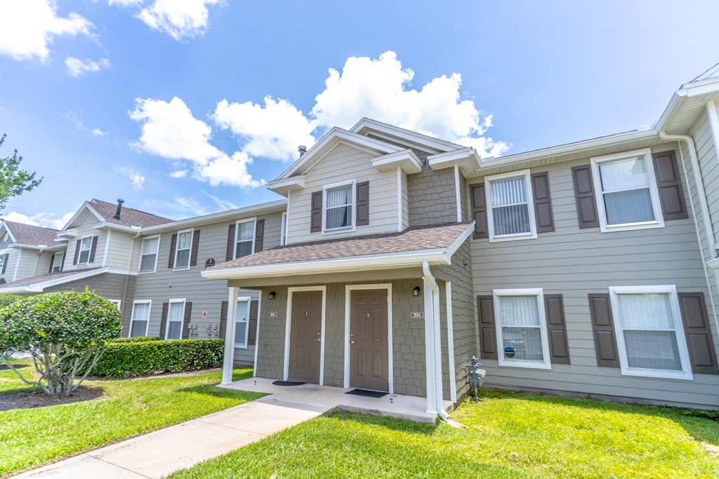 an apartment building with a grassy yard and a blue sky in the background