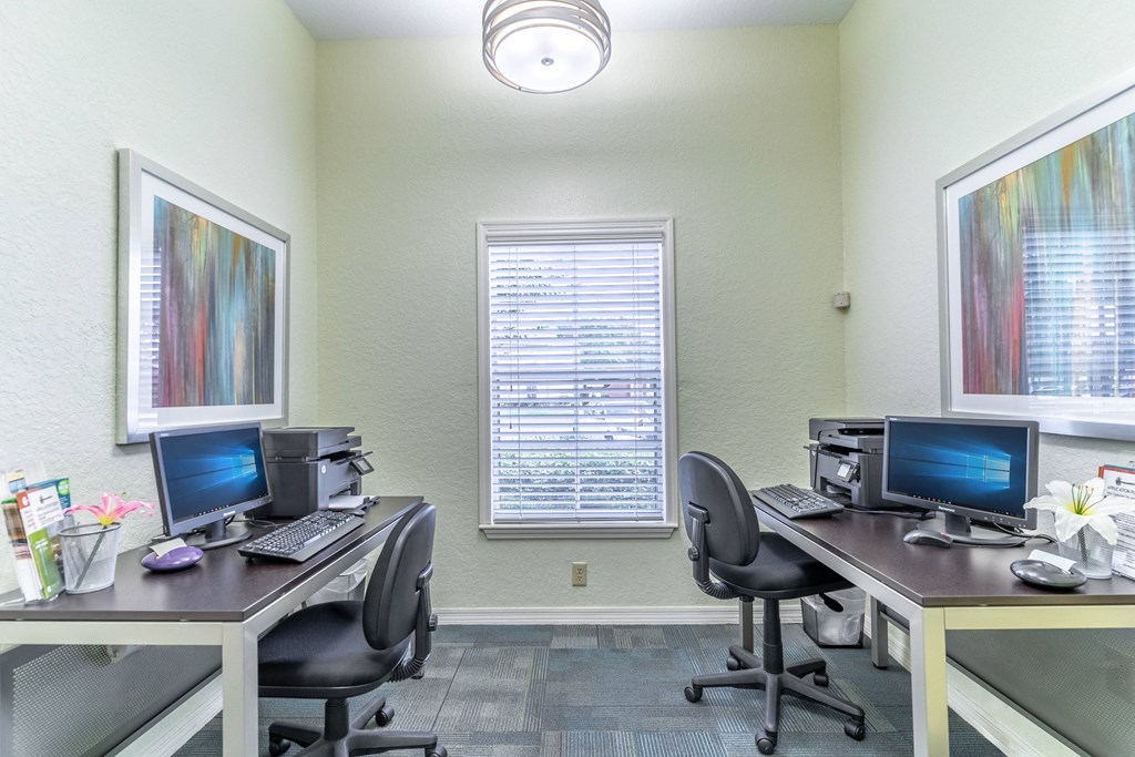 two desks with two computers and two printers in a room with a window
