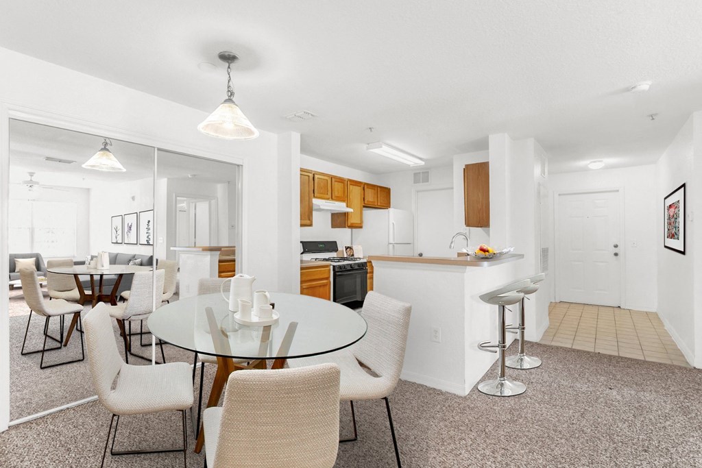 a dining area with a glass table and chairs and a kitchen in the background