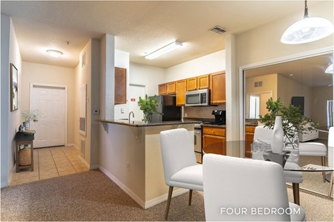 A kitchen with a dining table and chairs in a four bedroom apartment.
