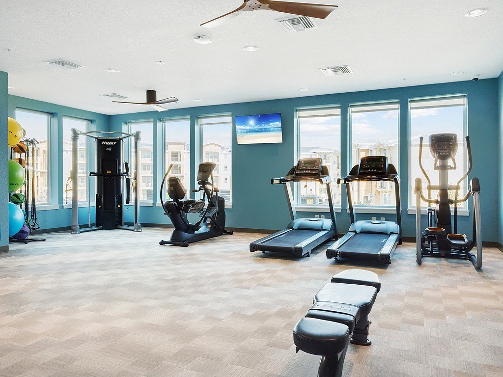 a fitness room with cardio equipment and windows in a building