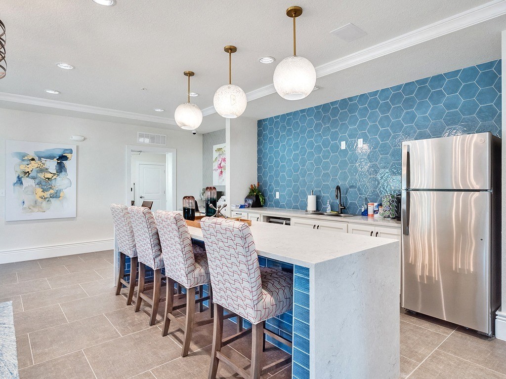a kitchen with a long island with bar chairs and a stainless steel refrigerator