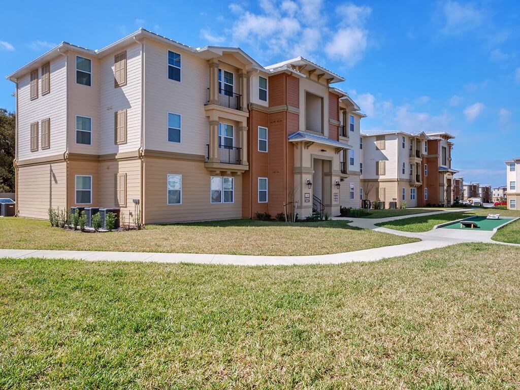 a row of apartment buildings with a sidewalk and grass