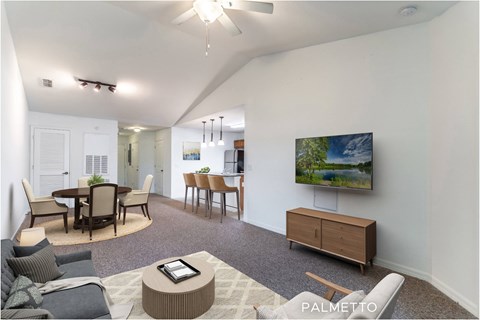 A living room with a grey carpet and a television on the wall.