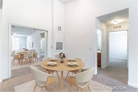A dining room with a table set for six with a view of the kitchen.