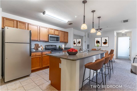 A kitchen with a refrigerator, microwave, and a counter with chairs.