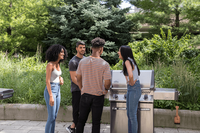 a group of people standing around a gas grill