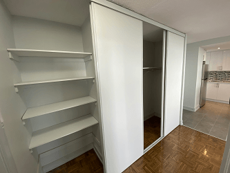 a walk in closet with white shelves and a mirrored closet door