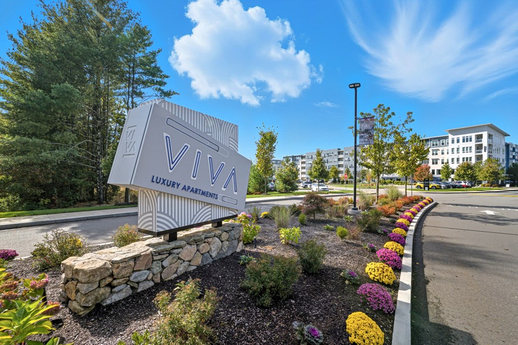 A sign for Viva Luxury Apartments is surrounded by a flower bed.