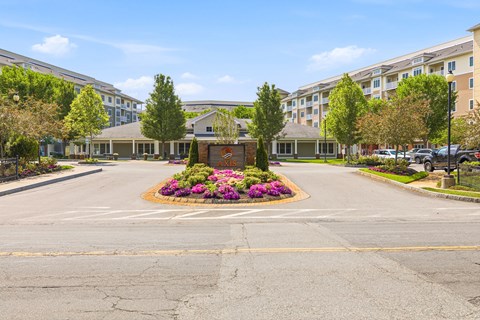 A sunny day at the entrance of a residential complex with a flower bed in the middle.