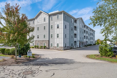 A large grey apartment building with a driveway in front.