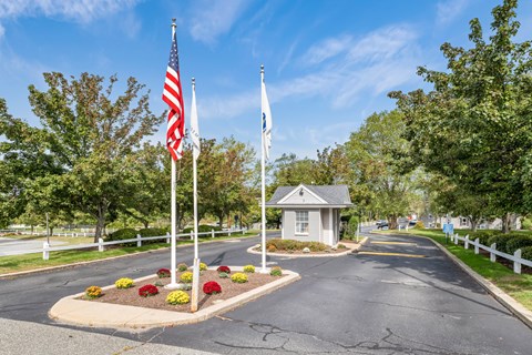 A road with a white fence and a small building with two flags on it.