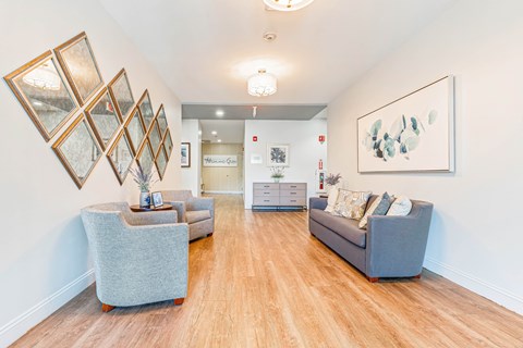 A living room with a grey couch, a grey ottoman, and a painting on the wall.